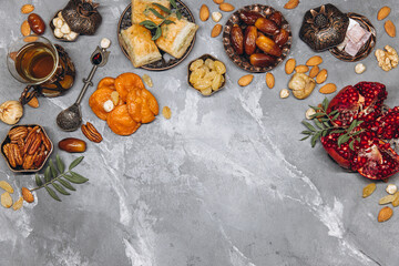 Stylish banner with traditional Arabic tableware and food sets, cup of tea, Koran and rosary on gray stone background. Ramadan table top view