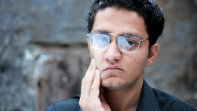Portrait shot of a young male with glasses looking tired and trying to look energetic. Tired student.
