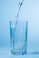 Water pours into a glass on a blue background. Clean drinking water