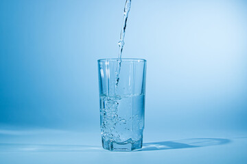 Water pours into a glass on a blue background. Clean drinking water