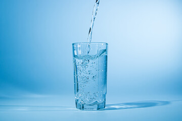 Water pours into a glass on a blue background. Clean drinking water