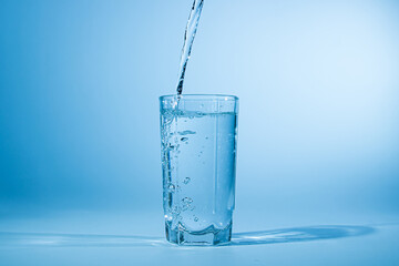 Water pours into a glass on a blue background. Clean drinking water