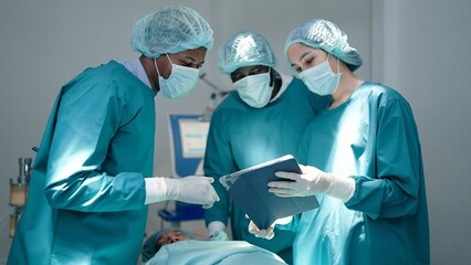 Professional surgeons and assistants talk and use digital tablet computer during surgery in the operating room modern hospital emergency departments