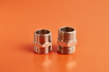 Double nipple with an external thread for connecting pipeline elements on an orange background. Plumbing and heating.