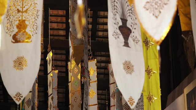 Many white ribbons with gold ornaments flutter in the wind in a Buddhist temple in Southeast Asia. Buddhist symbols Tung Lanna style decorations.