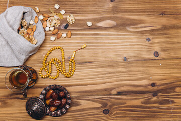 Ramadan concept, pouch with scattered nuts, plate of sweet dates and a cup of tea, top view and copy space