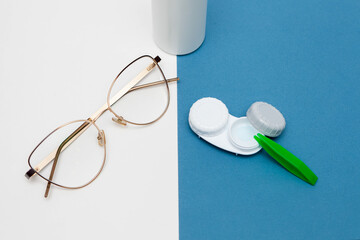 Container with contact lenses and glasses on a white and blue background, a bottle of contact lens...