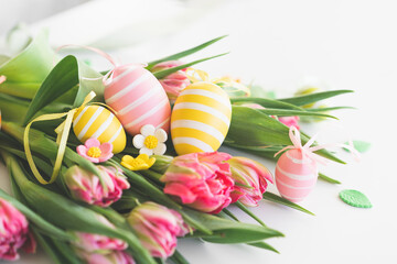 Obraz na płótnie Canvas Happy Easter. Stylish dyed easter eggs with spring flowers on white background. Pink tulips with colorful eggs