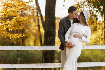 Happy stylish pregnant woman and man hugs, kiss, touches belly and listen baby's kicks, walk...