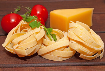 Dry nest pasta on a wooden table with tomatoes and cheese