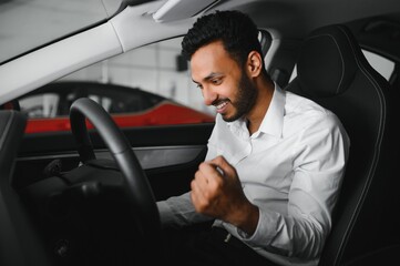 happy indian man checking car features at showroom