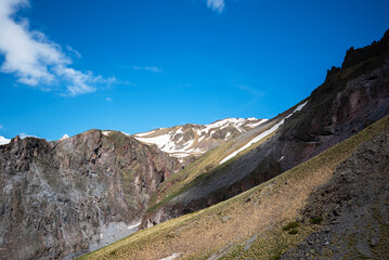 Summer landscape of a mountain peak with the remains of snow on the peaks. A stream of melted ice runs between the mountain slopes.