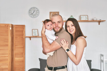 Obraz premium Young beautiful family. Mother and father hold newborn baby. Happy parents and child. Mother's and Father's Day