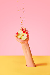 Closeup female hand with red painted nails squeezing half of apple fruit over pink yellow background. Contemporary art. Drops of juice fly up © Lustre