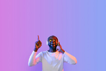 Excited african american man using headphones, pointing up