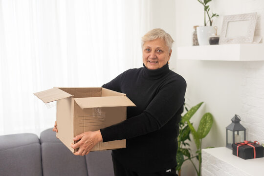 Smiling elderly woman customer receive post shipment parcel at home, happy old senior grandma hold open cardboard box sit on sofa in living room, online shopping order fast courier delivery concept.