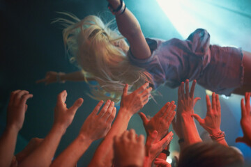 Surfing on a wave of fans. A young woman crowd-surfing at a concert. - obrazy, fototapety, plakaty