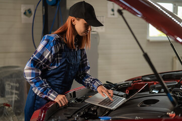 Obraz na płótnie Canvas Woman auto mechanic doing engine diagnostics using laptop. 
