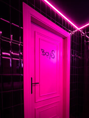 Pink door illuminated with neon and a painting of boys in dark corridor 