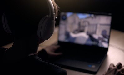 Young gamer is wearing a headset playing FPS video games at home. online video game technology concept. Teen boy play shooter video game on a mouse with a keyboard. Gambling addiction from video games