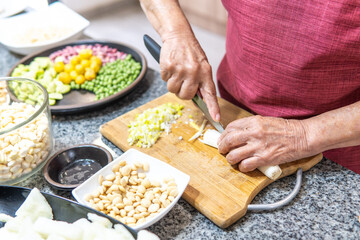 Hands of an elderly woman cutting onions with several legumes