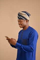 Portrait of handsome excited cheerful joyful delightful curious african guy wearing african attire, sending and getting messages to his lover isolated on brown background