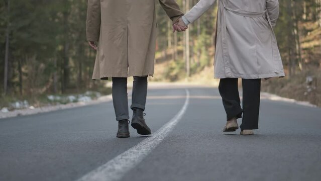 Romantic couple walking along highway in mountains forest. Man takes woman hand and romantic date outdoors. Joyful people boy and girl sit, walk on road. Love couple having fun while walking in nature