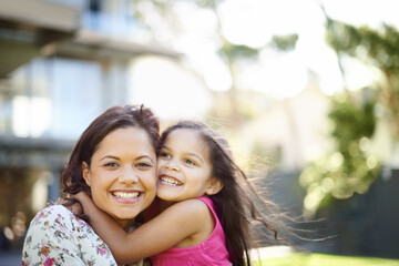 I love you mom. A cute little girl hugging her mom while they are standing in the garden.