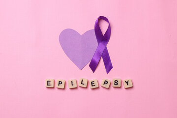 World epilepsy day. Purple heart shape and purple ribbon awareness with epilepsy lettering on pink background.  
