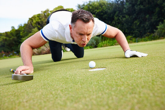 Its not cheating if nobody saw it. Shot of a handsome man trying to blow his golf ball into the hole.