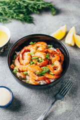 close-up of rice with fried shrimp and herbs next to sauce and lemon on a gray background