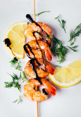 close-up on shrimp on a stick with lemon greens and soy sauce on a white background