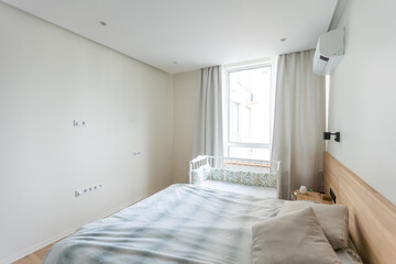 Bright and cozy modern bedroom interior with baby crib, white walls and a wooden parquet floor.