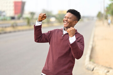 Handsome black african man celebrating winning with two power fist held up in the air on an african...