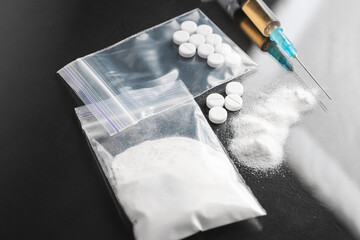 Hard Illegal drugs on dark background, cocaine or heroin white powder, white pills and syringe with a dose. Drug abuse and addiction concept