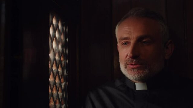 Catholic priest talking to parishioner in confessional booth. Pastor listening the confession in church. Clergyman giving advice to the churchgoer