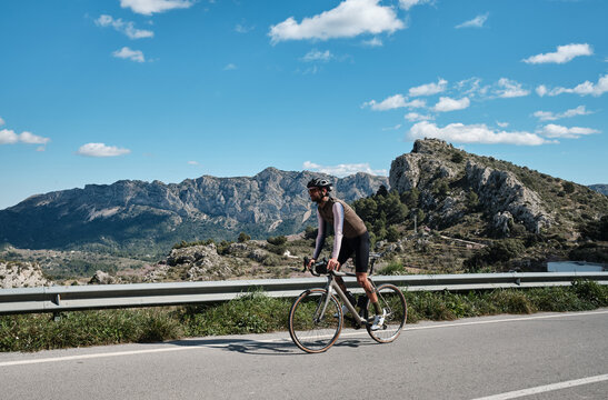 A cyclist is climbing up a mountain road on a gravel bike.A male cyclist is cycling in the mountains.Man cyclist  wearing cycling kit and helmet.Beautiful motivation image of an athlete.Spain