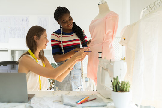 Two of young female dressmaker choosing colour samples fabric textile of dress on the dummy mannequin in tailor shop - Powered by Adobe