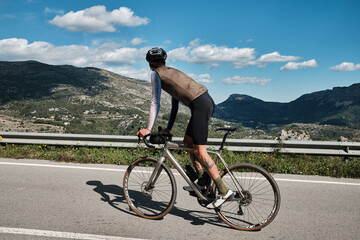 A man on a gravel bike is riding on the road in the hills with a view of the mountains.Sport motivation.Alicante region in Spain