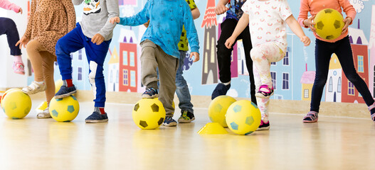 Children in kindergarten at soccer class. Group of kids with foam soccer football balls standing in line and kicking balls. Sports soccer training at kindergarten