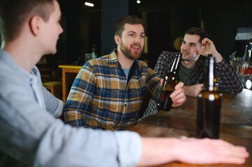 Young men in casual clothes are talking, laughing and drinking while sitting at bar counter in pub