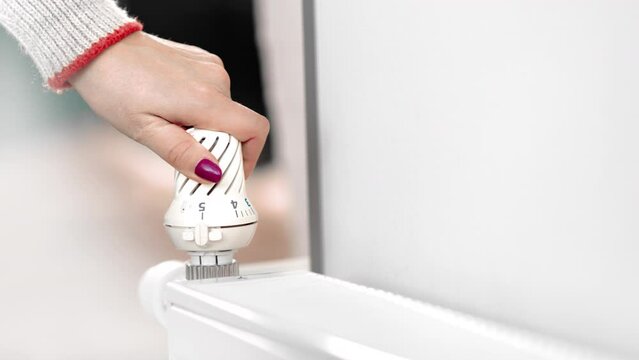 Heating home expensive cost woman hand adjusting temperature heat radiator warming control closeup