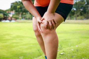 Obese woman knee pain after exercising outdoors on the lawn, massaging her legs with her hands....