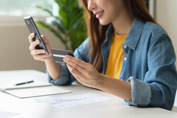 Online internet banking, smile asian young woman hand holding credit card to payment spending, using mobile phone scan qr code to transfer or pay money without cash at home. Technology of financial.