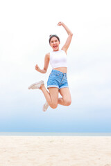 Obraz premium Cheerful young beautiful Asian woman having fun in white shirt and shorts jumping high on the beach. Smiling, happy to travel to the sea on weekends. travel concept