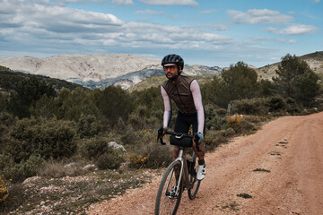 Fototapeta premium Fit male cyclist is riding dirt trails on a gravel bike. A man riding a gravel bike on a gravel road in a scenic view with hills in Castell de Castells,Alicante region, Spain. 