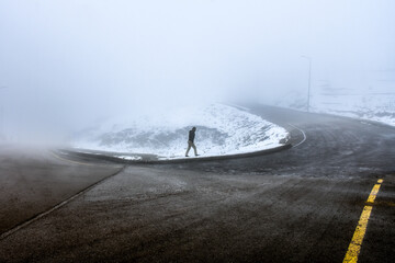 a man walks down a foggy bend and yellow road line seems