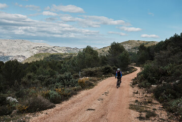 A woman cyclist is riding against a mountainous background.Female cyclist is riding a gravel bike on a gravel road.Cycling adventure. Parcent, Alicante, Spain