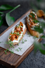 Bruschetta with chanterelles and Philadelphia cream cheese on a wooden board. Mushroom sandwich decorated with greens, selective focus
