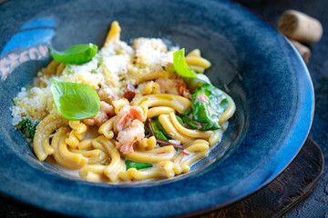 Cooking casarecce pasta with shrimp, basil and cream sauce in a blue plate. Italian dish casarecce seafood, close up
